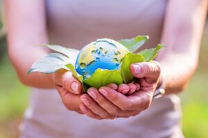 Young woman holding small planet in hands against spring or summer green background