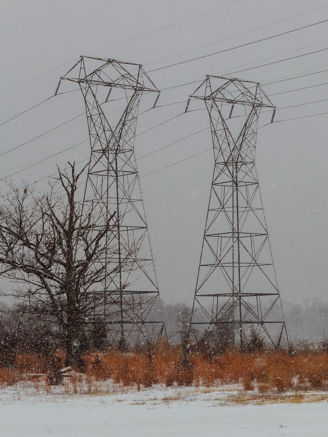 Power lines in winter scenery, electrical tower in wintertime with snow covered fields
