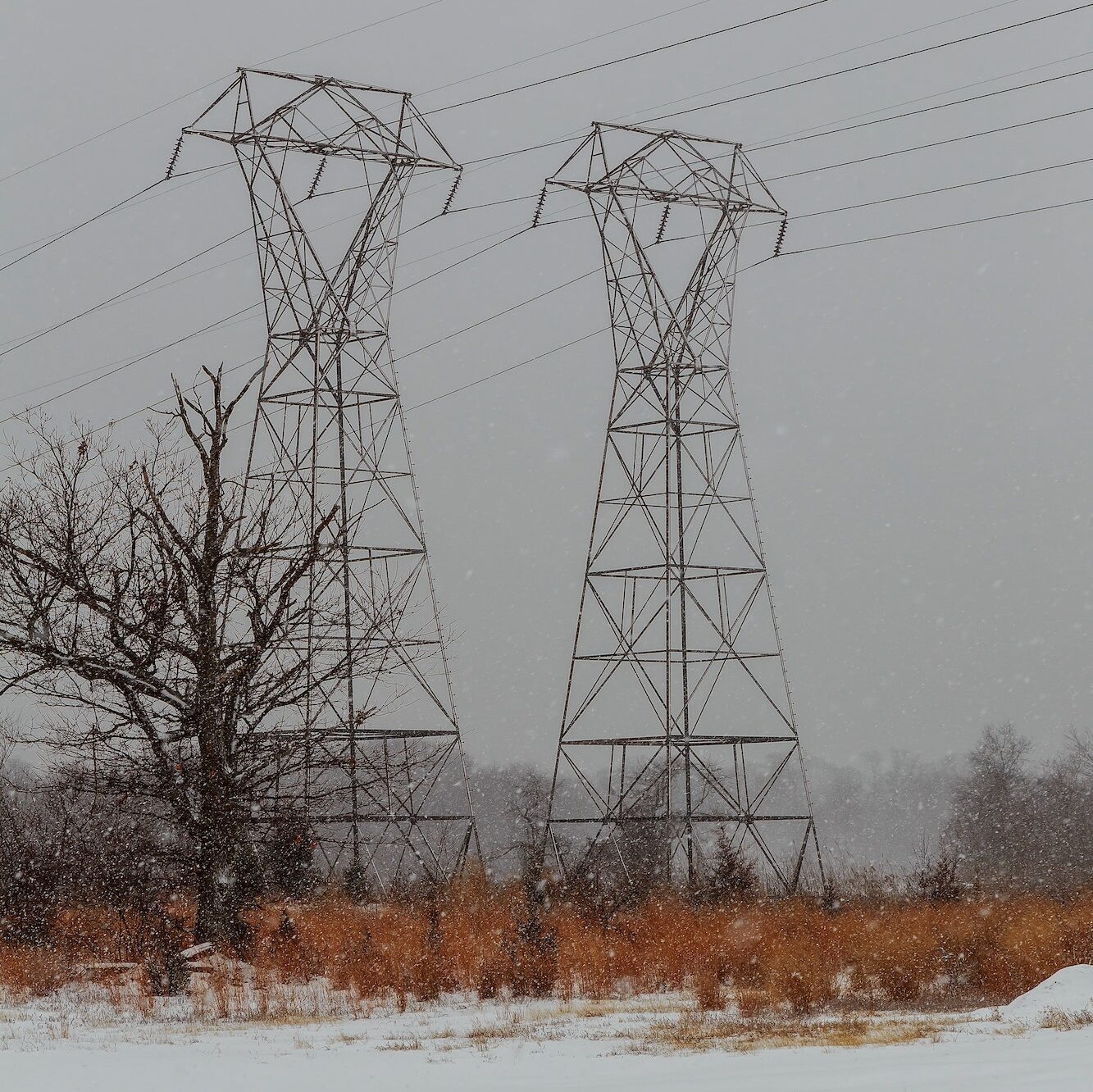 Power lines in winter scenery, electrical tower in wintertime with snow covered fields