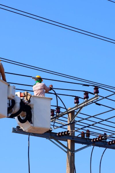 Two electricians on bucket boom truck installing electrical system on power pole against blue sky