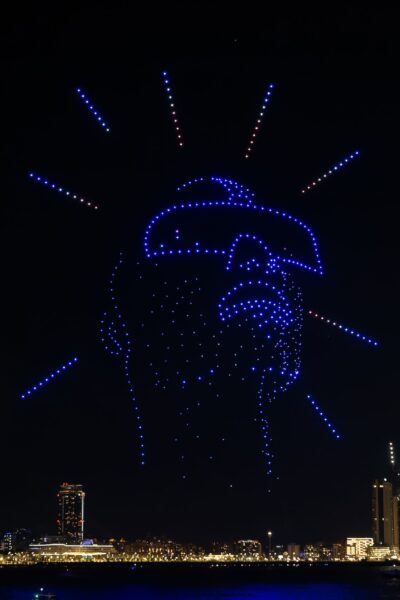 Illuminated blue drones glowing in the black night sky and forming a face with sunglasses