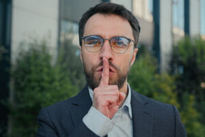 City portrait Caucasian business man businessman outdoors showing silence hush lips gesture keep